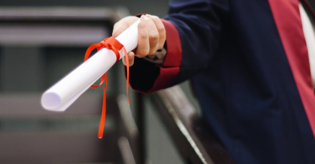 A close-up image of a graduate holding a diploma tied with a red ribbon, symbolizing achievement and success.