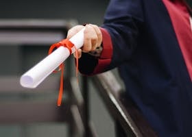 A close-up image of a graduate holding a diploma tied with a red ribbon, symbolizing achievement and success.